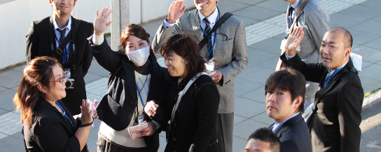 En gruppe japanske besøgende står udendørs og vinker til kameraet.